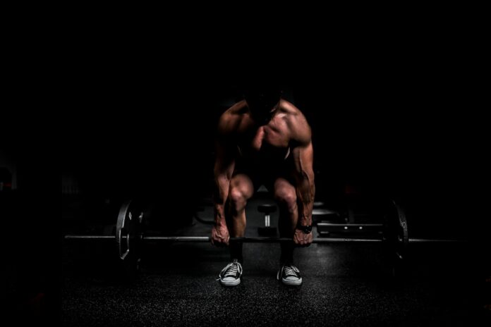 Photo by Anastase Maragos topless man in black shorts sitting on black and silver barbell