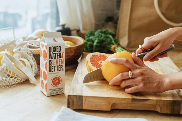 Photo by Boxed Water Is Better a person cutting an orange on a cutting board